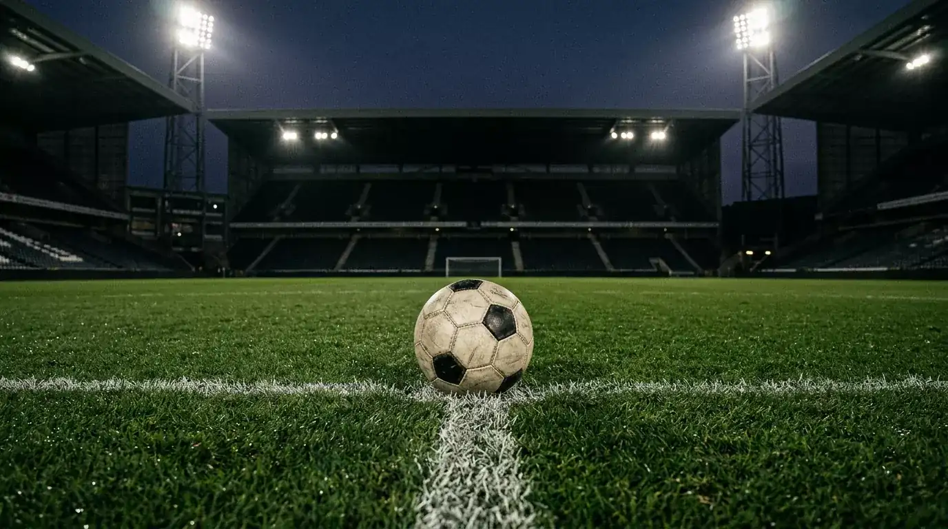 Balón de fútbol sobre el círculo central de un campo iluminado por focos nocturnos