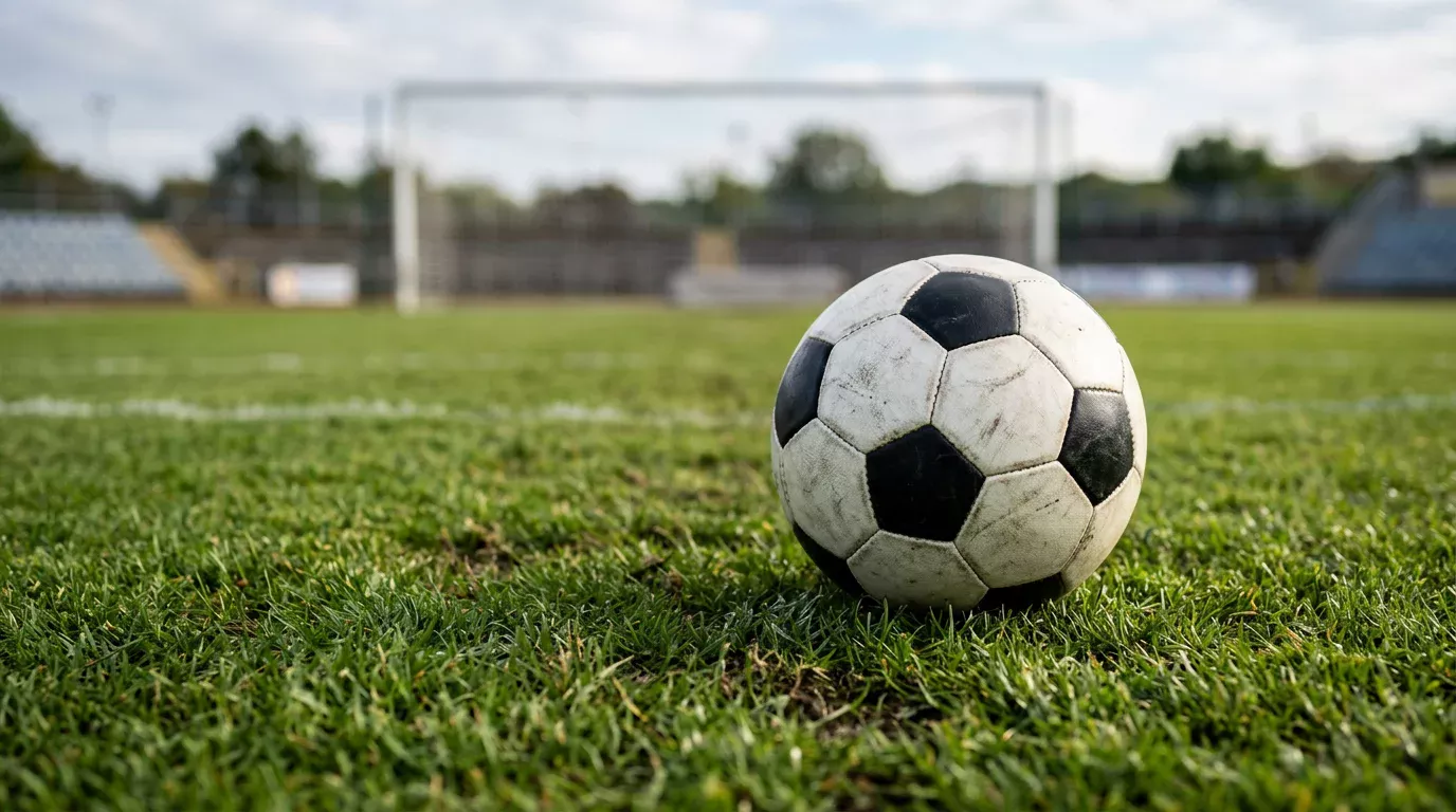 Balón de fútbol blanco sobre césped verde de un estadio con porterías al fondo